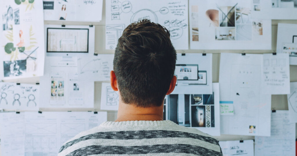 Man looking at a bulletin board full of notes and diagrams.